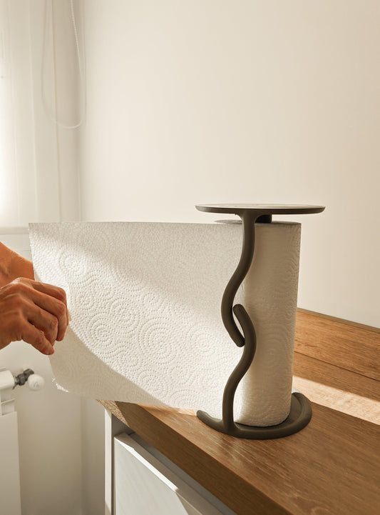 Person using a paper towel roll on a stand with a white wall background