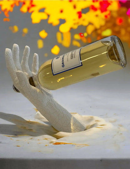 Bottle of white wine labeled 'Grand Reserve' held by a white hand sculpture on a white surface with colorful blurred background.