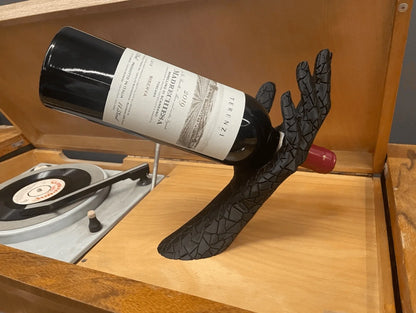 Wine bottle held by a black lace glove on a wooden surface with a record player in the background.