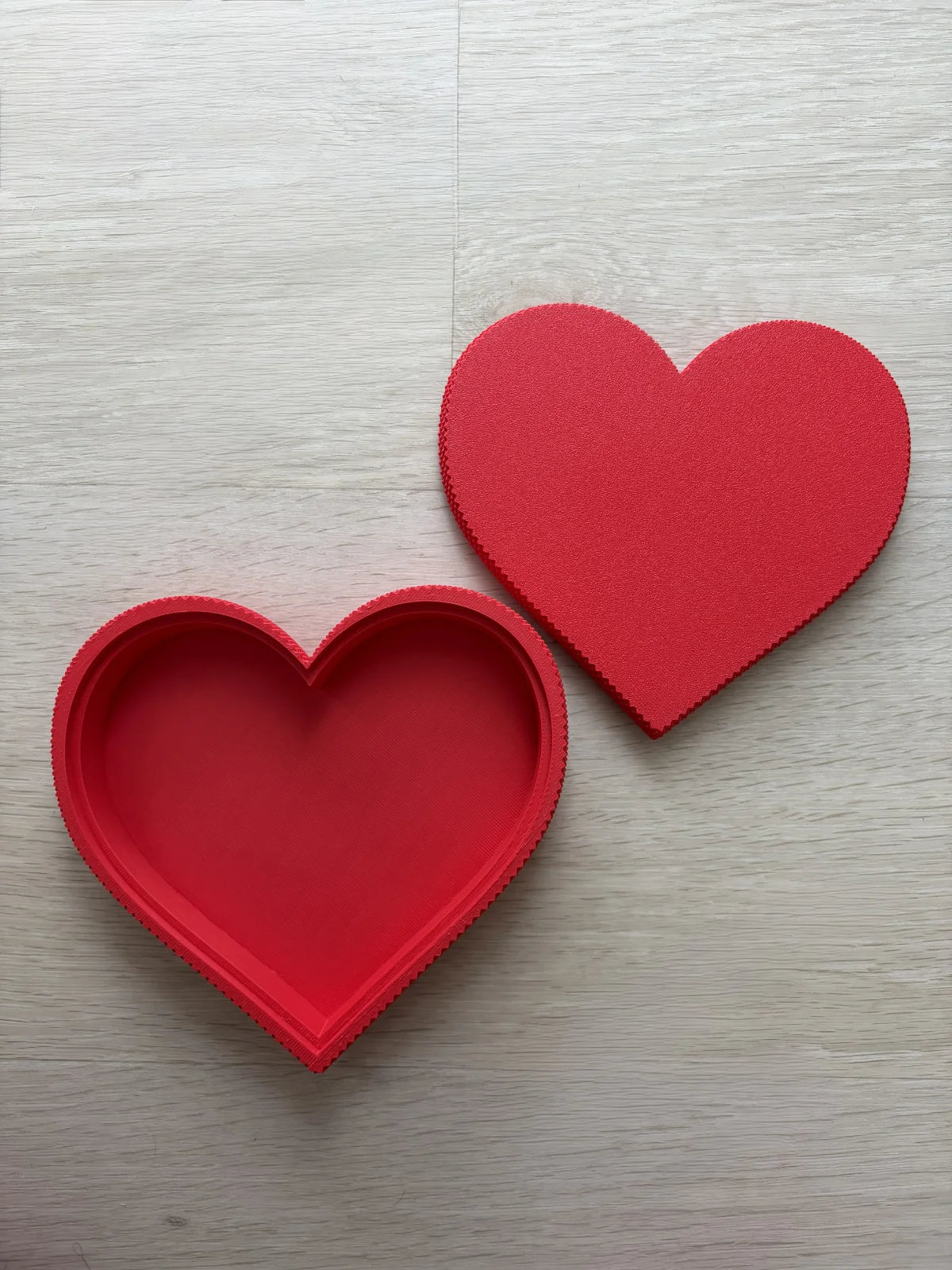 Two red heart-shaped objects on a light wooden surface