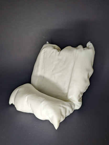 White ceramic sculpture of a chair on a dark gray background